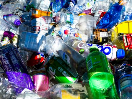 A crowded pile of mixed plastic bottles and cans, many crushed and sparkling with condensation, suggesting collected recyclables.