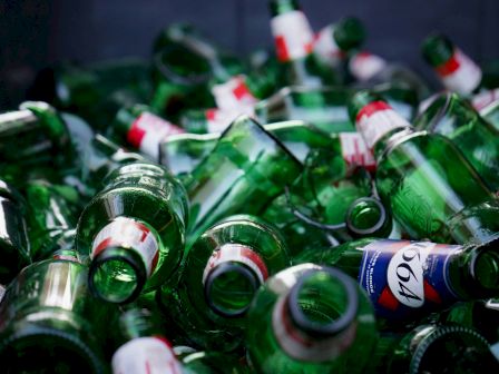 A cluttered pile of empty green glass bottles and cans, likely beer, scattered and stacked after a party.