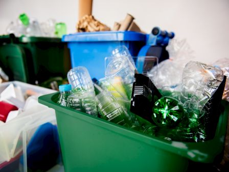 A recycling bin full of plastic bottles and glass containers, with cardboard and cans in the background.